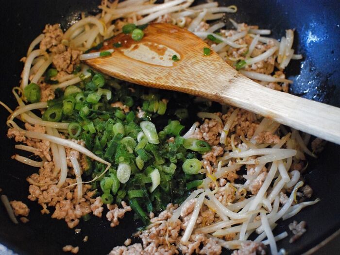 炒めた豚ひき肉ともやしに、ネギを加えます