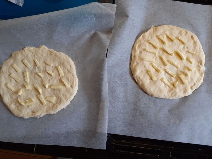 ①クッキングシートに（一次発酵させた）フランスパン生地を丸く平に伸ばしバターをのせる（2枚作る）