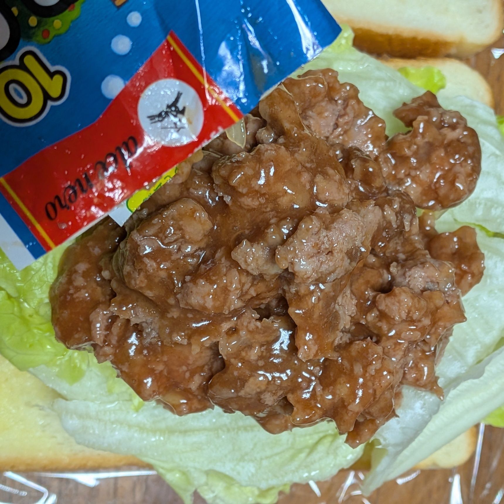 6. ミートボールを袋の上から手で潰し、レタスの上に絞り出す。パン一面に広げる。