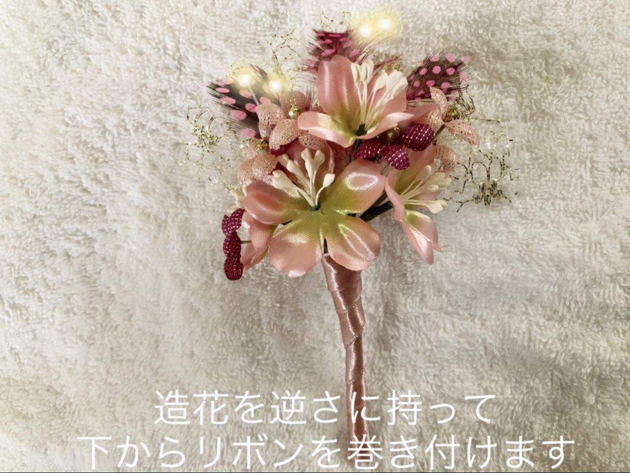 造花を逆さに持って、茎の下からリボンをくるくると巻いていきます