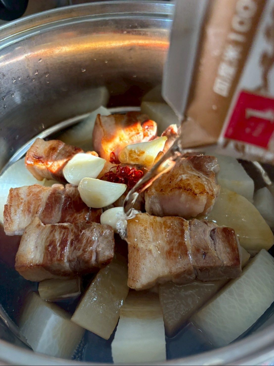 大根の上にバラ肉とニンニク、唐辛子を乗せてお酒をかけて蓋をして煮ます。