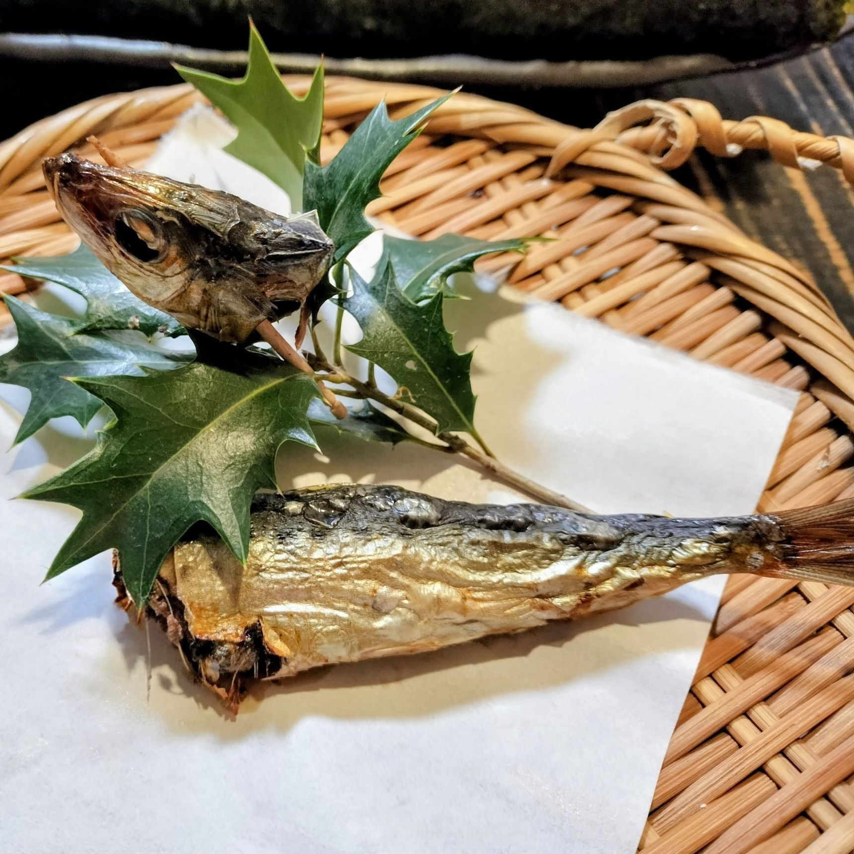 2. 籠（皿）に、天ぷら紙を敷く→節分ヒイラギをのせ、爪楊枝を刺した目刺しの頭を添える→目刺しの身をのせる