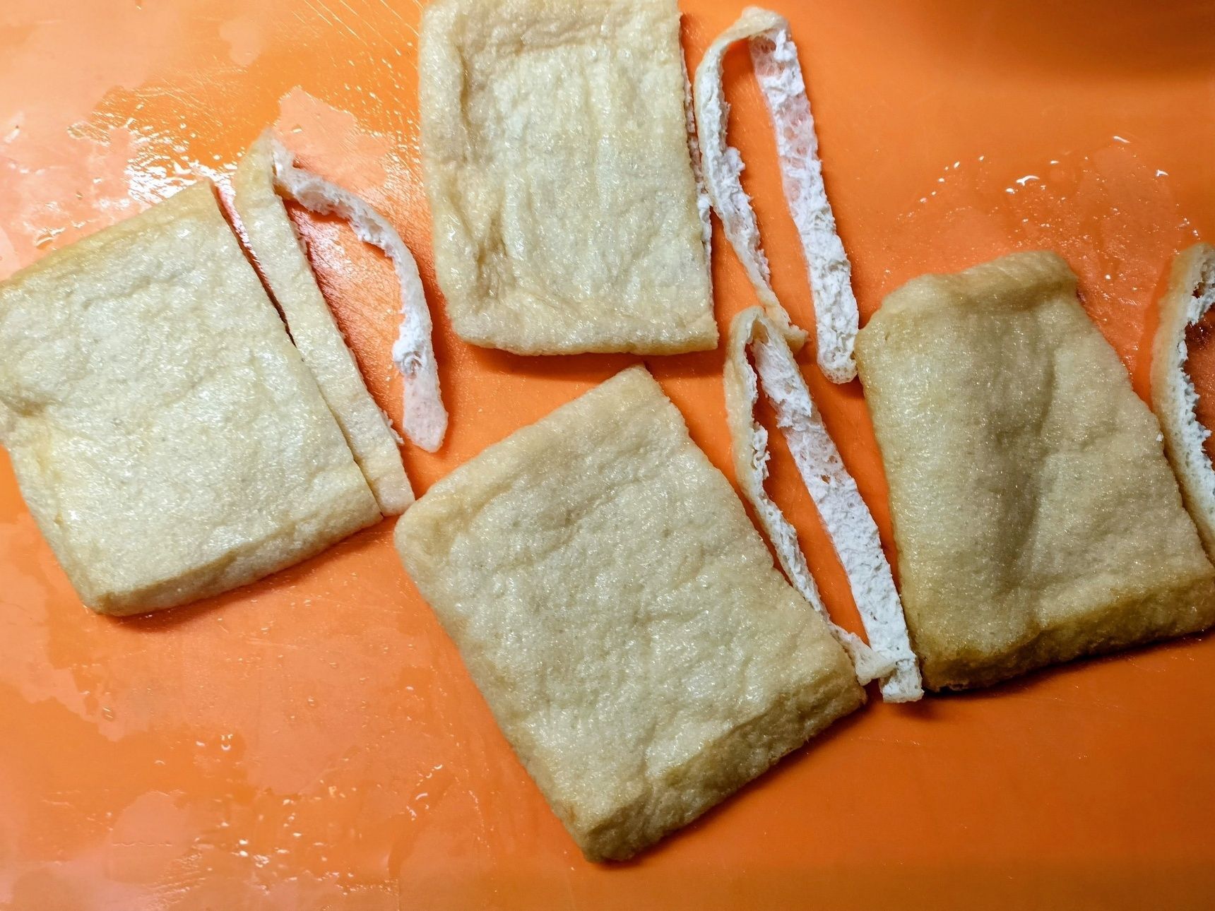 2、耐熱皿に油揚げを入れる→少量のお湯を加えて、電子レンジで1分ほど加熱する→ザルにあける→両手で優しく挟んで水気を絞る→下画像のように切る