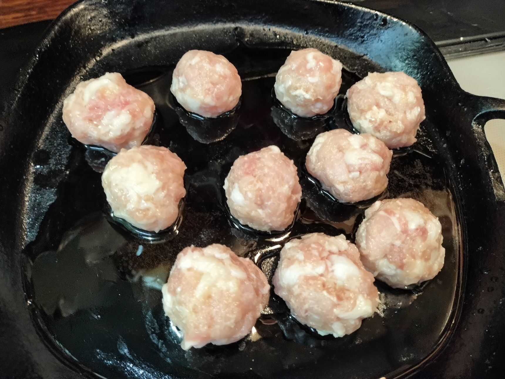 3. 手順2の豚ロース肉に片栗粉を加えて、しっかりと揉み込む→鉄フライパンに、おおよそで10等分に分けながら、肉団子を作って並べる→ごま油を回し入れる→中火で片面に焼き色をつけ、ひっくり返す→軽く押さえて少し平らにして、焼き色をつける→蓋をして、中まで火を通す→蓋を取り、中火で両面をカリッと焼く