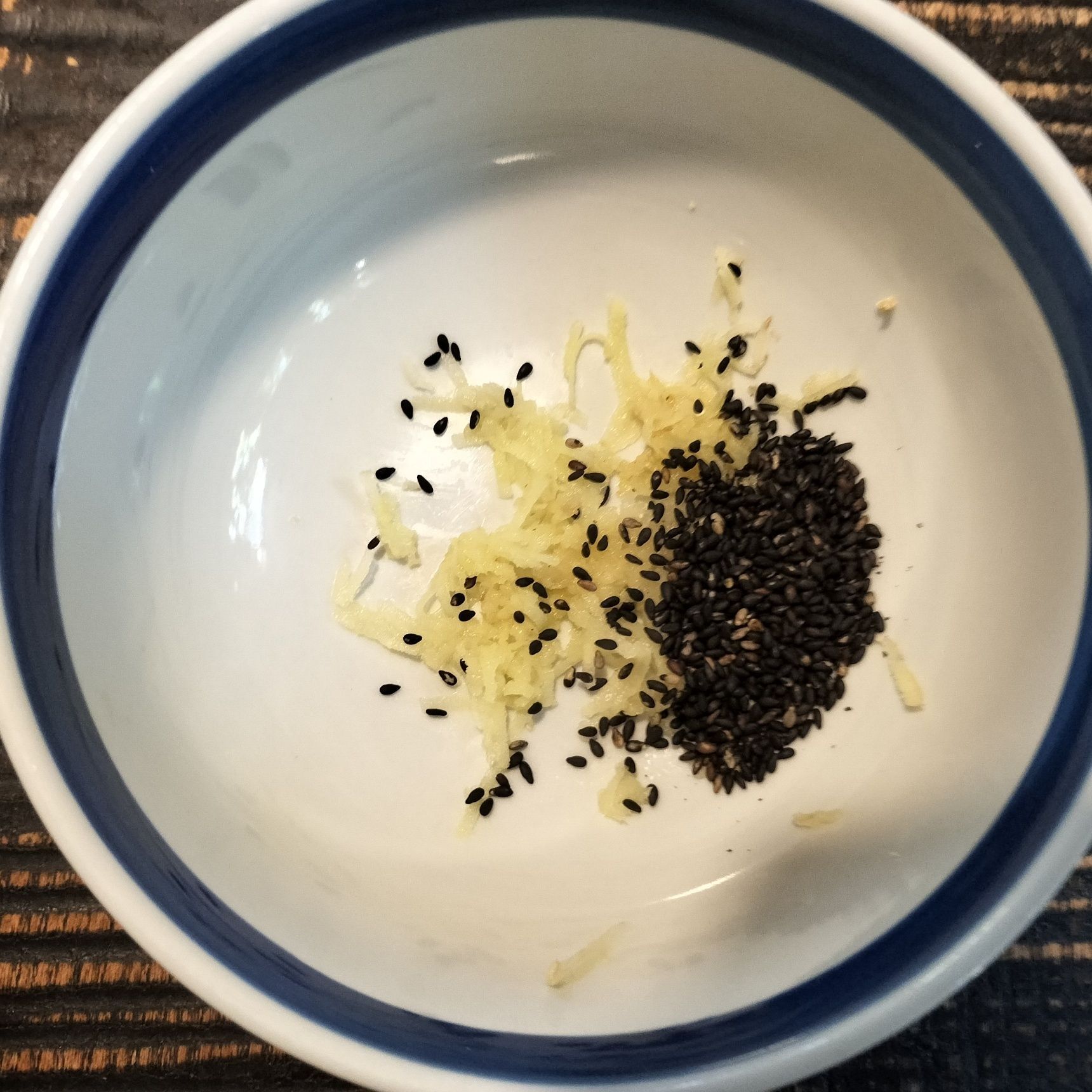 1、器に、すりおろした谷中生姜と黒胡麻を入れる→炊きたての白飯を加える→温かいうちに切るように混ぜる→粗熱をとる