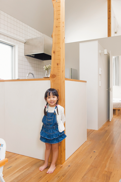 大黒柱にとりつけた天然木の身長計とその前に立つ女の子